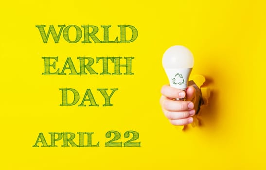 A person holding a light bulb with the words World Earth Day on the background. The image is yellow and green