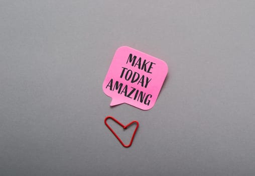 A pink sticky note with the words Make today amazing written on it. A red paper clip is placed on the note