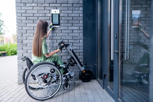 A woman in a wheelchair with an assistive device for manual control enters the entrance. Electric hand bike