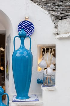 Beautiful view of an old tall blue jug standing on a small ledge on the shelf of a white house during the day in the city of ostuni, puglia, italy, close-up side view.