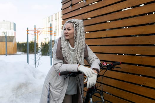 A woman is actively pedaling a bike down a street covered in snow, surrounded by cold winter scenery. She is bundled up in warm clothing, focused on navigating the slippery path.