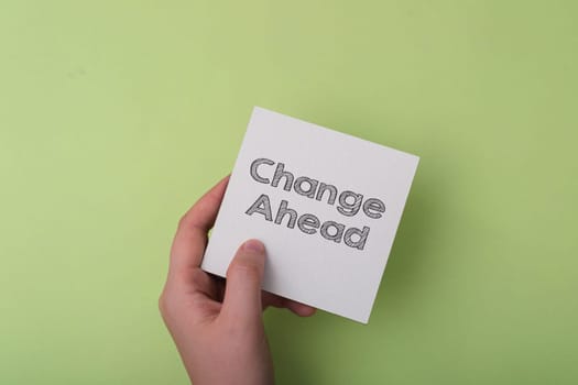 A hand holding a white card with the word change ahead written on it. The card is on a green background