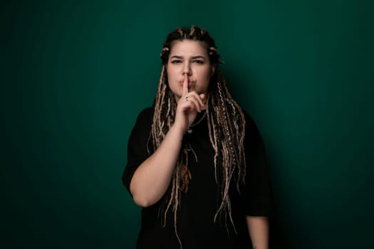 A woman with dreadlocks is shown in the photo, pressing her index finger to her lips in a hush gesture. Her facial expression is serious and focused.