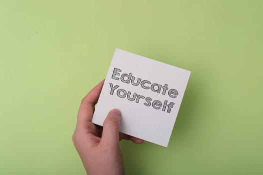 A hand holding a piece of paper with the words educate yourself written on it. The image conveys the importance of self-improvement and learning