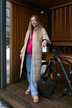 A woman is standing next to a bike on a wooden platform. She is wearing casual clothing and appears to be preparing to ride the bike.