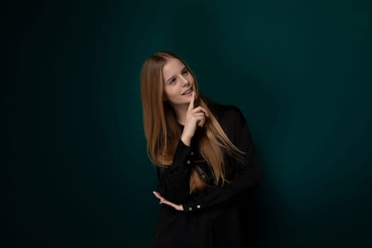 A woman standing in front of a solid green wall, looking directly at the camera. She appears calm and composed, with a neutral expression on her face.