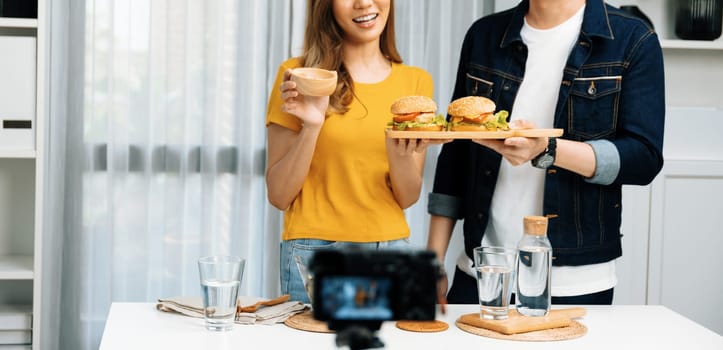 Cropped photo of chef influencers presenting on cooking show on social media channel serving double big hamburger with dressing camera recording. Bun bread wholegrain and salad placing menu. Infobahn.