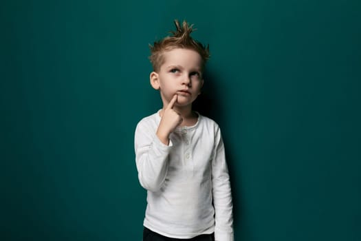 A young boy is seen standing in front of a bright green wall. The boy appears curious and engaged, looking directly at the camera. The wall provides a bold backdrop for the boys presence.
