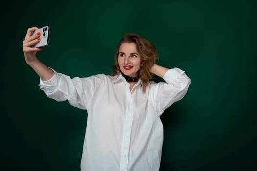 A woman holding a cell phone in front of her, smiling as she takes a selfie. She is standing outdoors, likely in a city setting, capturing a moment of self-expression.