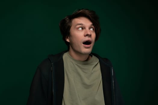 A male individual is standing in front of a vibrant green background, with a look of genuine surprise on his face.