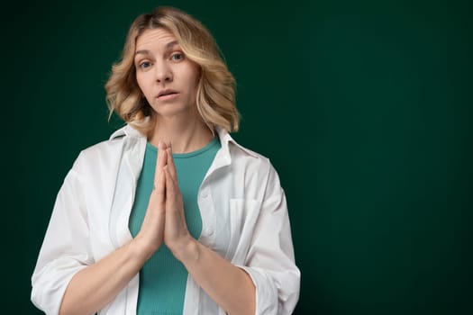 A woman wearing a white shirt is shown praying with her eyes closed and hands clasped together. She appears to be focused and deep in prayer.