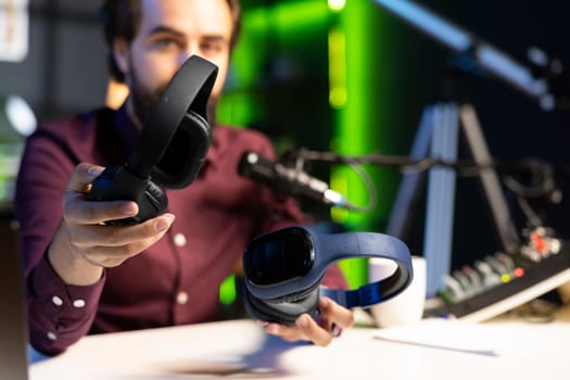 Close up shot of newly launched wireless headphones reviewed by man comparing features with older models. Focus listening devices analyzed by technology internet show host in blurry background