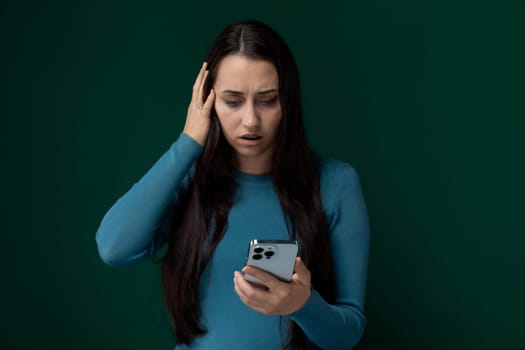 A woman wearing a blue shirt is seen holding a cell phone in her hand. She appears focused on the screen, perhaps texting or browsing. The background is neutral, allowing the woman and her phone to be the center of attention.