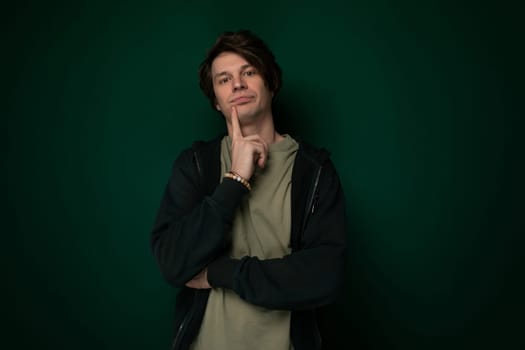 A man is standing upright in front of a green wall. He appears calm and is looking directly ahead. The wall behind him is a solid shade of green and provides a simple background.