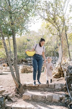 Mom with a bowl helps a little girl down the stone steps in the park. High quality photo