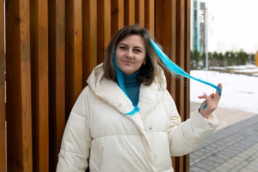 A woman is wearing a white jacket and has a blue scarf on her head. She appears stylish and confident, walking or standing in an urban setting.