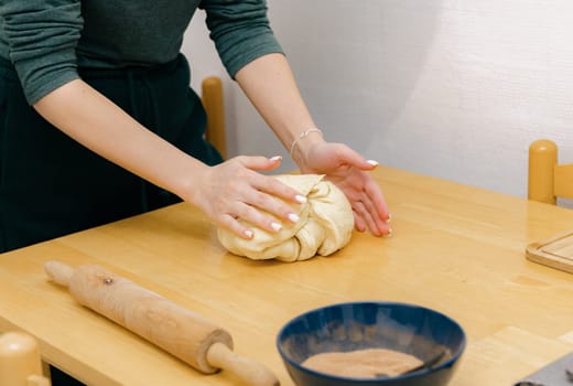 One young Caucasian unrecognizable girl kneads yeast dough with both hands on a wooden table, standing in the kitchen, close-up side view. Step-by-step instructions for baking synabons. Step 4.
