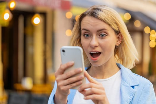 Oh my God Wow. Excited happy joyful winner young woman using smartphone looking at screen browsing celebrating win good message news. Caucasian lady traveler with mobile phone in urban street outdoors