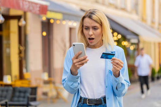 Shocked Caucasian woman trying to pay online shopping with smartphone blocked credit card. Annoyed lady tourist on street buying bank refuse problem unsuccessful payment lack of money balance bankrupt