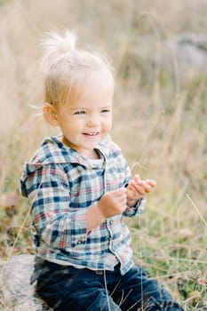 Little smiling girl sits in a clearing and holds a blade of grass in her hands. High quality photo