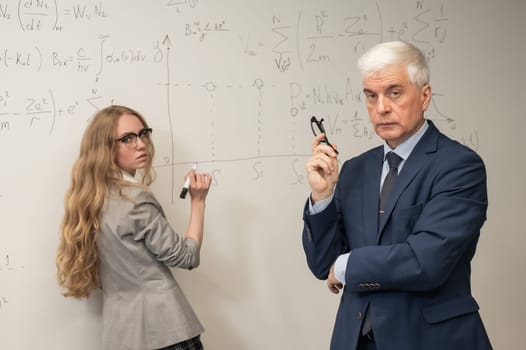 Female student answers a question from an elderly professor at a white board