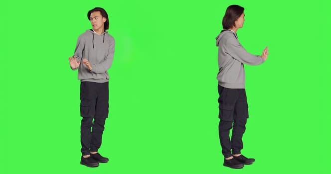 Person pretending to push thing aside, expressing rejection or denial in studio. Young adult mimicking refusal over isolated full body greenscreen background, stop symbol on camera.