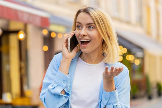 Caucasian woman tourist having remote conversation communicate speaking by smartphone with friend, talking on phone unexpected good news gossip walking on urban city street. Town lifestyles outdoors