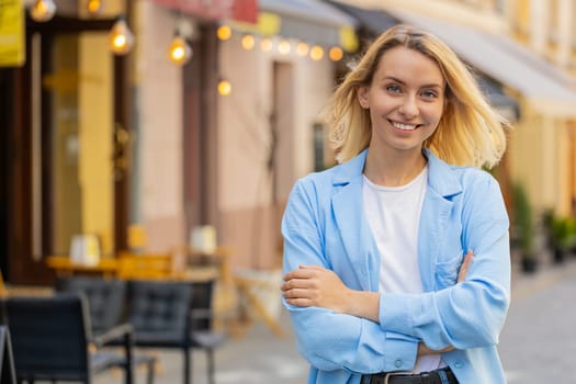 Portrait of happy young blonde woman friendly smiling glad expression looking at camera dreaming resting relaxation satisfied of good news outdoors. Lady standing on urban city street. Town lifestyles