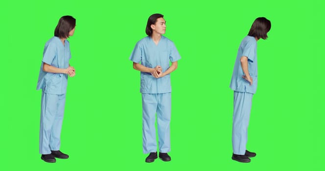 Over greenscreen wall, healthcare worker awaits for event, dressed in hospital protective outfit and being anxious. Man with medical expertise and natural abilities stands in studio.