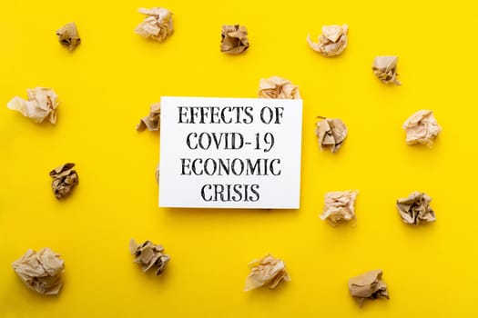 A yellow background with a white sign that says Effects of COVID-19 Economic Crisis. The sign is surrounded by crumpled paper