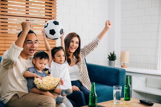 A jubilant family watches a football match with popcorn and a ball, raising arms and celebrating. Their togetherness and cheers reflect the joy of winning and their shared love for the sport.