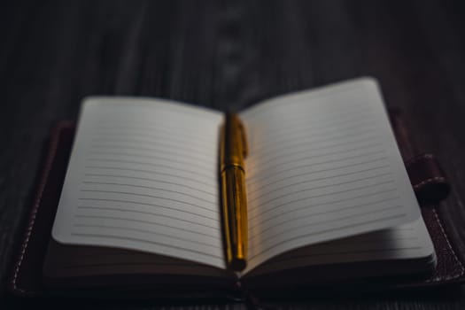 A notebook with a gold pen on the table in the candlelight. High quality photo