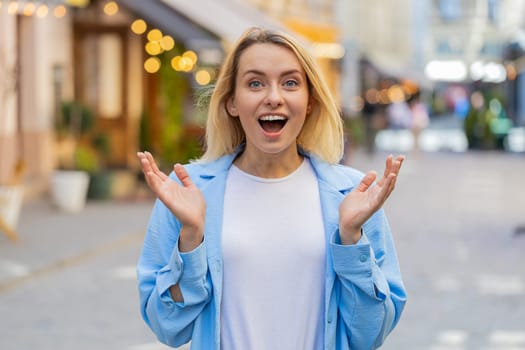 Oh my God, wow. Caucasian young woman looking surprised at camera with big open eyes shocked by sudden victory, game winning, lottery goal achievement, good news outdoors. Lady on city sunshine street