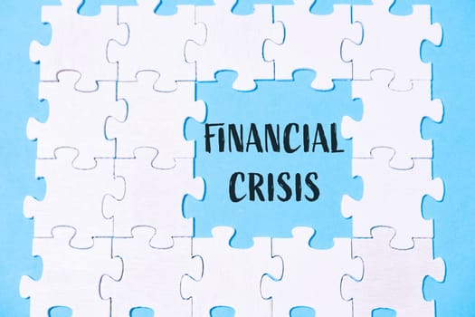 A jigsaw puzzle with the word financial crisis written in the middle. The puzzle is made up of white pieces and is on a blue background