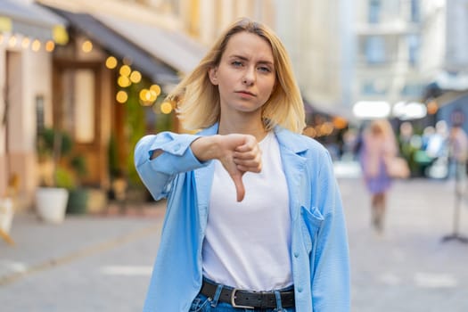 Dislike. Upset Caucasian woman showing thumbs down sign gesture, expressing discontent disapproval dissatisfied bad work mistake. Displeased lady female standing on urban city sunshine street outdoors