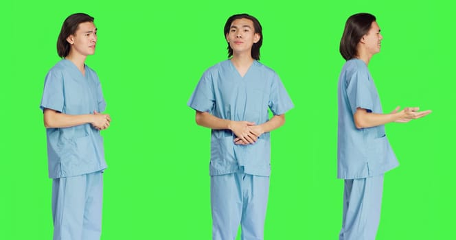 Friendly nurse waving on camera and greeting patients, standing over greenscreen background. Young medical specialist being respectful and confident in his abilities, healthcare uniform.