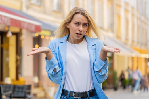 I don't know what to say. Confused young woman feeling embarrassed about ambiguous question having doubts no idea being clueless uncertain outdoors. Caucasian adult lady standing in urban city street