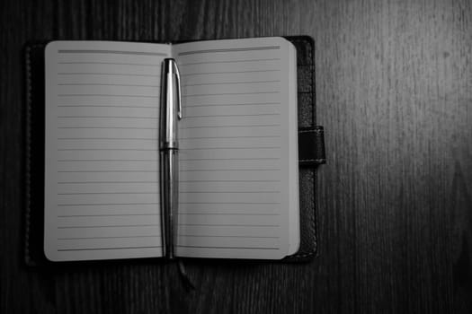 Black and white photo of the notebook with a pen on the table in the candlelight. High quality photo