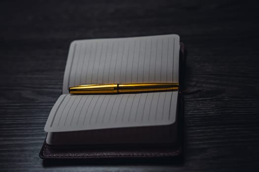 A notebook with a gold pen on the table in the candlelight. High quality photo