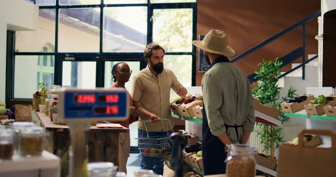 Couple asking vendor about fresh produce in organic zero waste store, storekeeper recommending fruits and veggies harvested from garden. Merchant presenting chemicals free food.