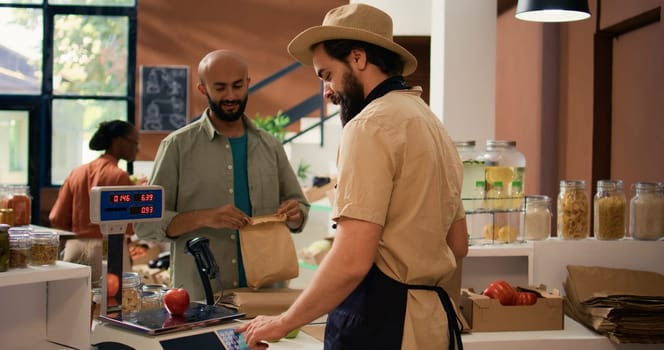 Local vendor weighting goods at checkout cash register, using electronic scale to determine weight and cost. Young storekeeper encouraging healthy eating and vegan sustainable lifestyle.