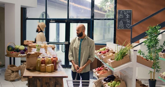 Middle eastern client looks at produce on local grocery store shelves, living vegan lifestyle and searching for bio organic fruits and veggies. Young man checking pasta and grains in jars, bulk items.