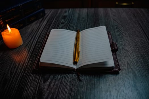 A notebook with a gold pen on the table in the candlelight. High quality photo