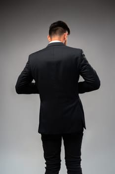 Young businessman from the back standing on gray background in studio