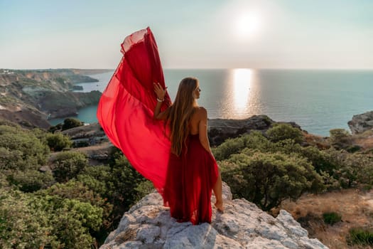 Woman sunset sea red dress, back view a happy beautiful sensual woman in a red long dress posing on a rock high above the sea on sunset