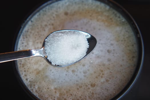 dropping sugar from a spoon in a coffee cup