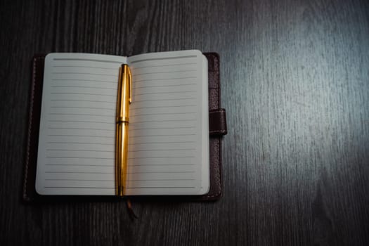 A notebook with a gold pen on the table in the candlelight. High quality photo