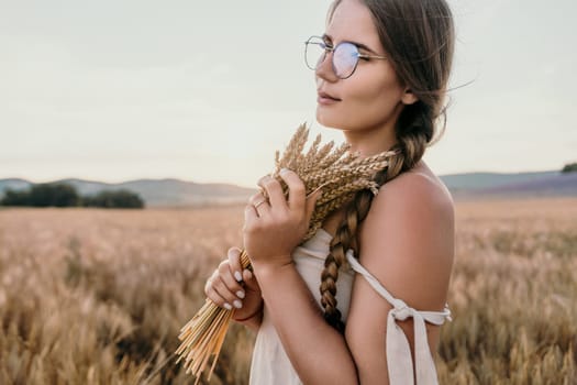 A woman is holding a bunch of wheat in her arms. The wheat is dry and brown, and the woman is wearing a white dress. The scene is set in a field, and the woman is posing for a photo