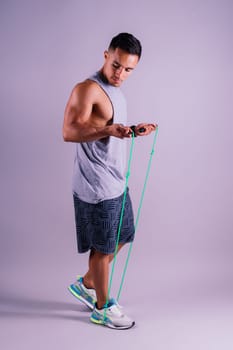 A man with a grey tank top is holding a green jump rope with his elbow bent and waist twisted, showing off his toned chest and wrist strength