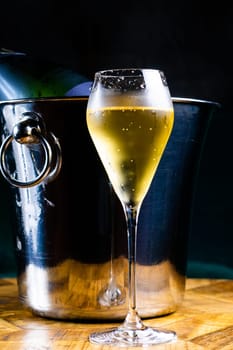 Bottle and cup of champagne on a wooden table, dark background